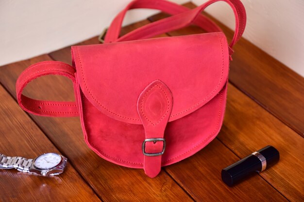 Photo sac rouge en cuir pour femmes à la mode sur un fond en bois, près d'elle une montre et un rouge à lèvres