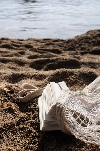 Sac shopping en filet écologique et un livre près de la mer sur une plage de sable