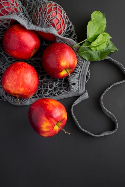 Sac shopping en filet gris avec des pommes rouges sur fond noir Pas de concept de sac en plastique Vue de dessus Emplacement vertical