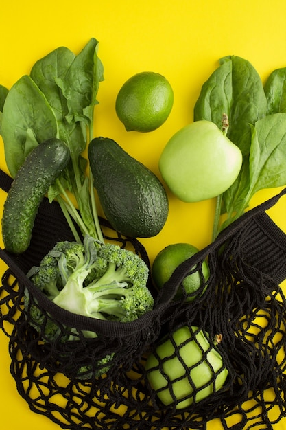 Sac shopping noir en filet avec fruits et légumes verts sur le jaune