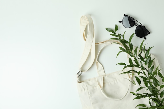 Sac textile vierge, branche et lunettes de soleil sur une surface blanche