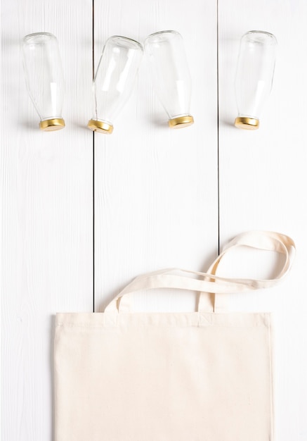 Un sac tissé réutilisable repose sur une surface blanche avec des bouteilles en verre à côté.