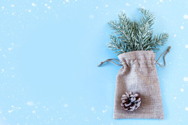 Photo sac en toile avec branches d'épicéa et pomme de pin sur fond bleu. notion de noël et du nouvel an. mise à plat, vue de dessus, espace de copie.