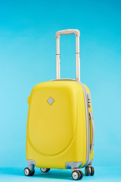 Sac de voyage coloré jaune avec poignée sur roues sur fond bleu