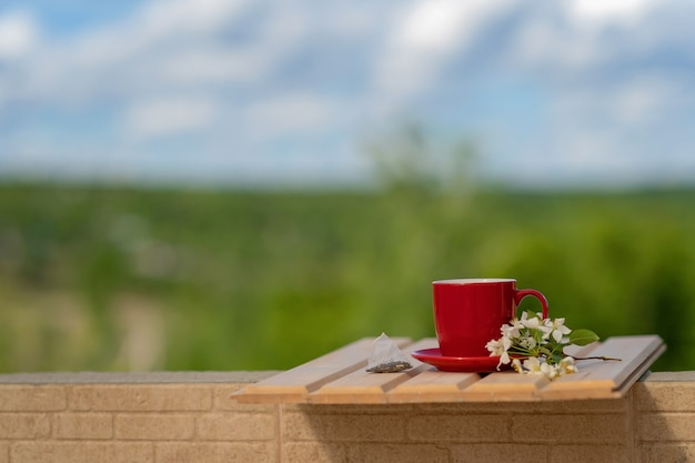 un sachet de thé jetable à côté d'une tasse rouge et d'une branche de pommier en fleurs sur une table en bois