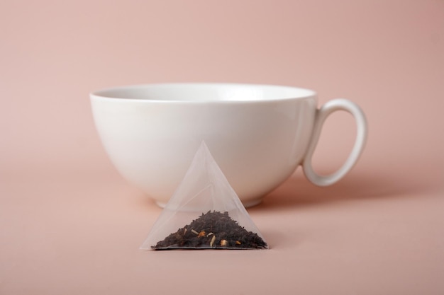 Sachet de thé triangulaire et tasse en céramique blanche sur fond beige