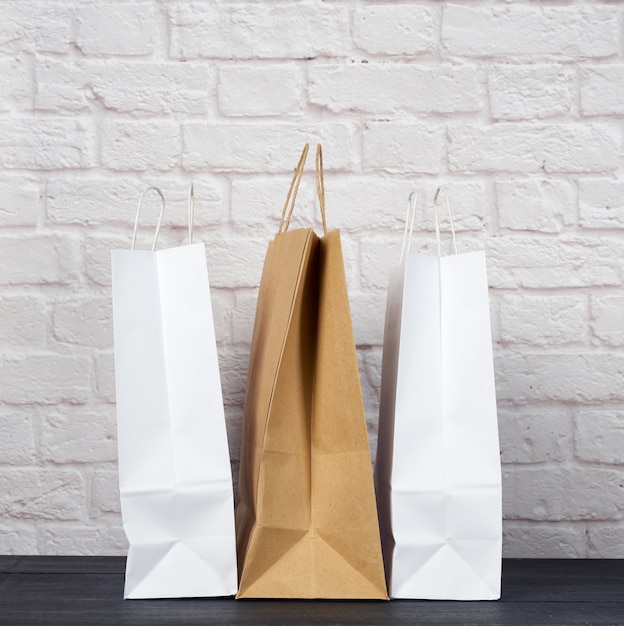 Sacs en papier blanc et brun avec poignées sur fond de mur de brique blanche