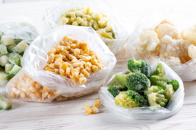 Photo sacs en plastique avec des légumes surgelés sur table en bois blanc
