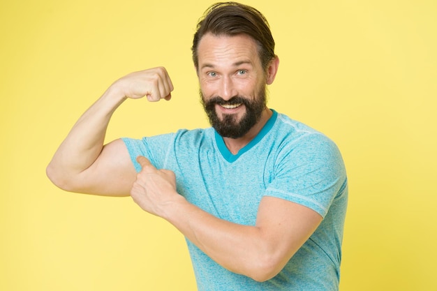 Sain et heureux. Un mode de vie sportif et une bonne nutrition aident à garder la jeunesse et la fraîcheur même à un âge mûr. Homme à la barbe pointant vers ses biceps de bras musclés. Mode de vie sain, clé de la vie à l'infini.