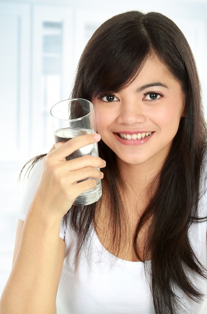 Saine jeune femme tenant un verre d'eau et souriant