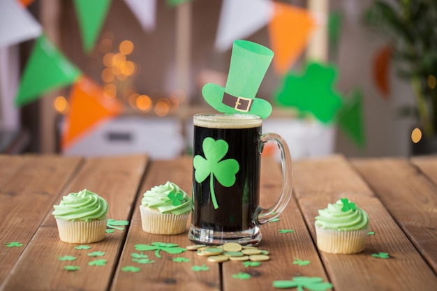 Saint-Patrick's Day vacances et célébration concept verre de bière foncée avec des cupcakes verts et des pièces d'or sur une table en bois