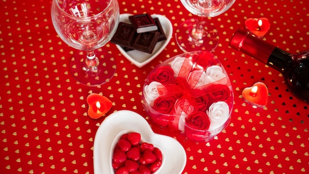 La Saint-Valentin. Bouteille de vigne, verres, roses rouges, bougies - fond rouge. Concept de dîner d'amour