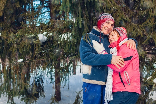 La Saint-Valentin. Couple de famille senior étreignant dans la forêt d'hiver. Heureux homme et femme marchant à l'extérieur.