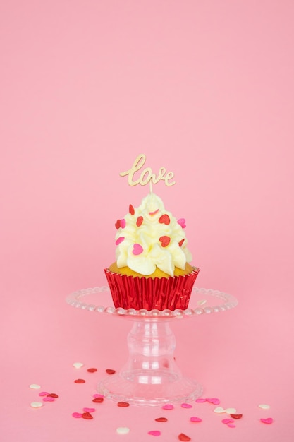 La Saint-Valentin. Un cupcake à la crème et à la décoration rouge avec un panneau en bois avec le mot LOVE sur fond rose.Photo verticale. Espace de copie.