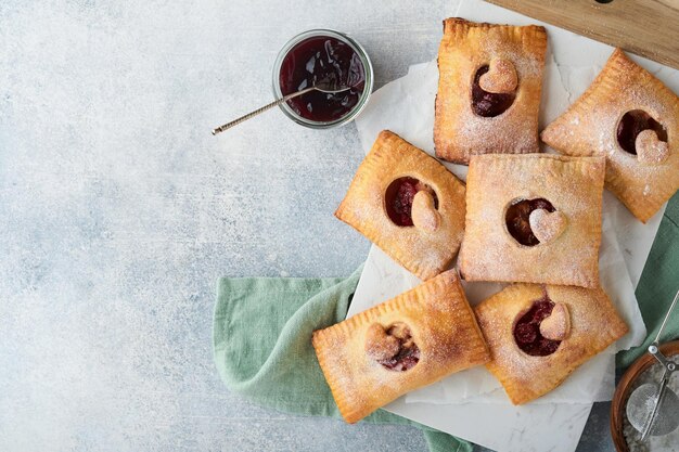 Saint Valentin en forme de coeur Tartes à la main Mini pâte feuilletée ou tartes à la main farcies de pomme et saupoudrer de sucre en poudre dans l'assiette Idée de collation romantique maison Saint Valentin Vue de dessus Espace de copie