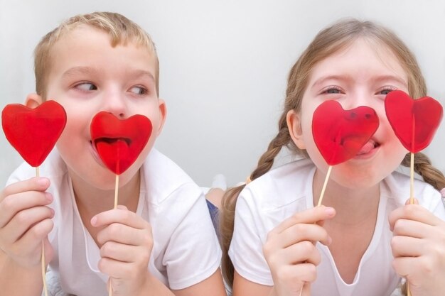 Photo saint valentin un garçon et une fille mangent des sucettes caramel rouge en forme de coeur