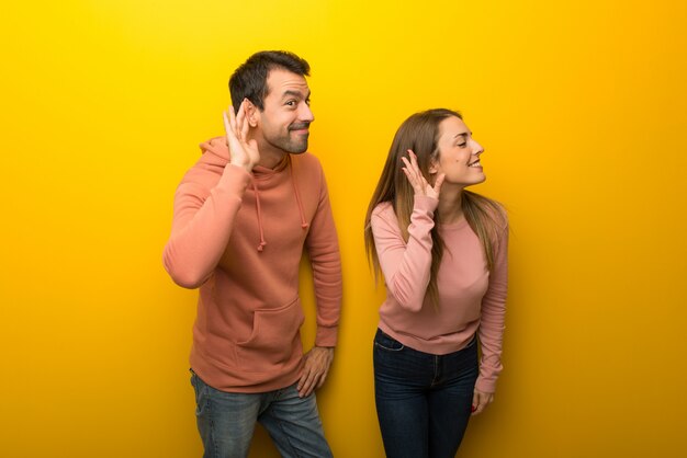 À la Saint-Valentin Groupe de deux personnes sur fond jaune écoutant quelque chose en mettant la main sur l&#39;oreille