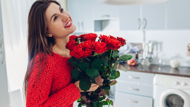 La Saint-Valentin. Jeune femme a trouvé un bouquet de roses rouges dans la cuisine. Fille heureuse tenant des fleurs.