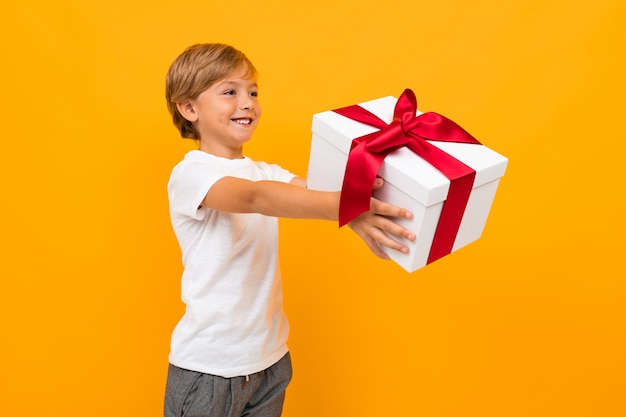 La Saint-Valentin . joli garçon tend une boîte avec un cadeau avec un ruban rouge sur un jaune vif