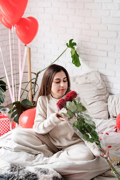 Saint Valentin, Journée de la femme. Jeune femme brune caucasienne assise dans le lit célébrant la saint valentin sentant les roses rouges