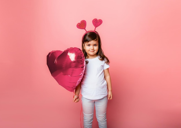 Saint Valentin Petite fille tenant un gros ballon en forme de coeur sur fond rose