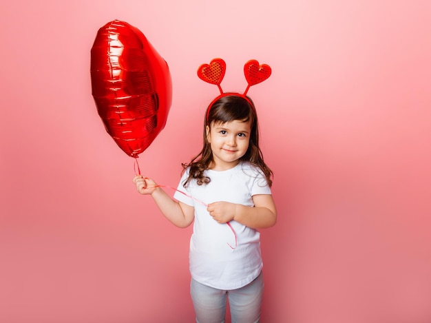 Saint Valentin, petite fille tenant un gros ballon en forme de coeur sur fond rose.