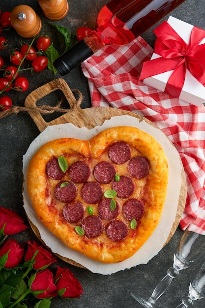 Saint Valentin pizza en forme de coeur avec mozzarella pepperoni et basilic bouteille de vin deux verres à vin coffret cadeau sur fond noir Idée pour un dîner romantique Saint Valentin Vue de dessus Maquette