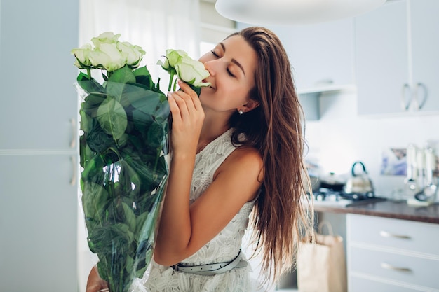 Saint valentin présente heureuse jeune femme sentant le bouquet de fleurs de roses le jour de la femme de cuisine