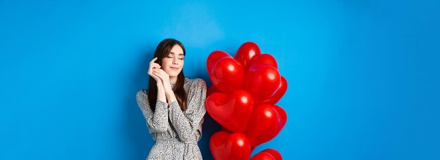 Saint valentin rêveuse femme romantique fermer les yeux et imaginer une belle date debout près des ballons cardiaques