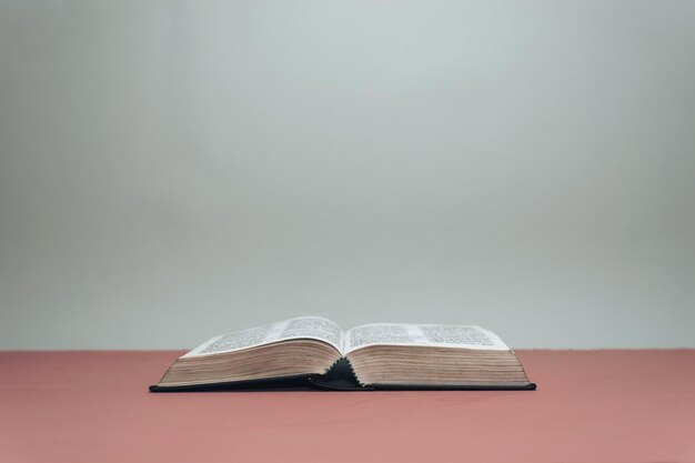 La Sainte Bible ouverte sur une table rouge Fond de mur gris