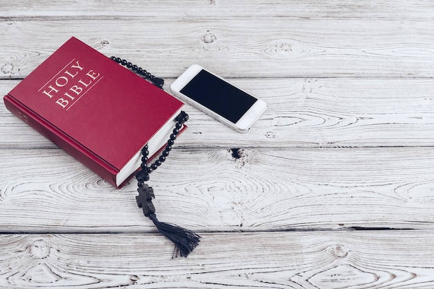 Sainte Bible et smartphone avec une tasse de café noire sur une surface en bois.