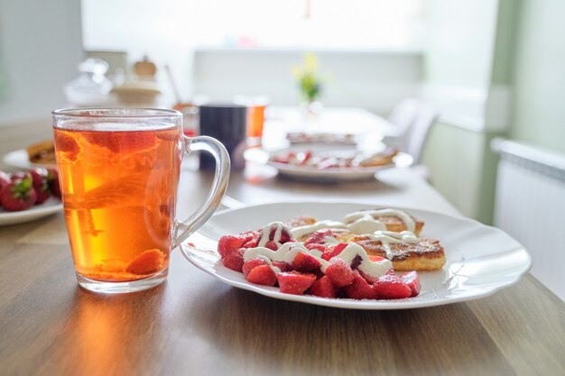 Saison des fraises, nourriture et boisson avec des baies. Nourriture sur la table, crêpes au caillé avec fraises et crème sure. Thé au citron et aux baies