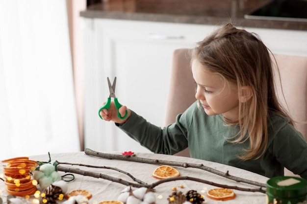 Saison des vacances d'hiver enfant petite fille en bas âge faisant des décorations de maison de guirlande de Noël faites à la main à partir de matériaux naturels ECO