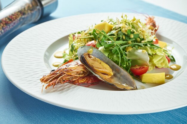 Salade appétissante aux fruits de mer, langoustines ou crevettes, moules, roquette et tomates cerises dans une assiette blanche sur nappe bleue