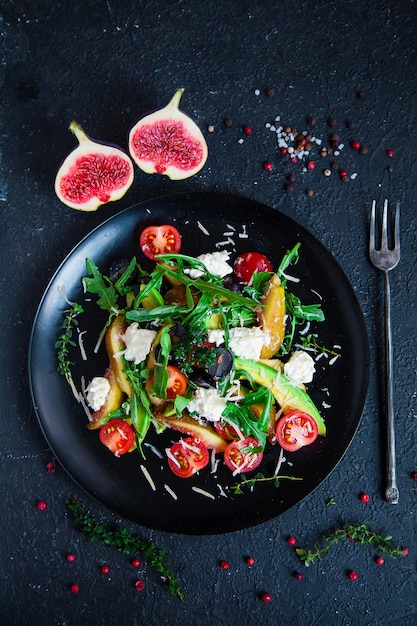 Salade sur assiette: roquette, tomates cerises, figues blanches, fromage râpé, raisins noirs