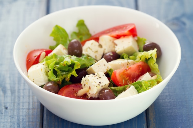 Salade au fromage avec des légumes dans un plat blanc sur fond bleu