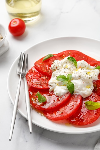 Salade au fromage Stracciatella sur plaque blanche avec huile de fourchette basilic frais et tomates Close up