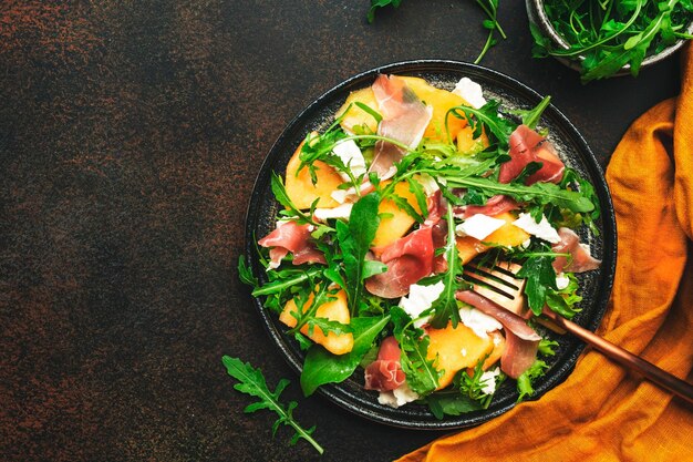 Salade au melon jamon fromage de chèvre et roquette sur fond marron vue de dessus copie espace