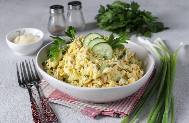 Salade au poulet chou chinois concombre oeufs durs et fromage dans un bol blanc sur fond gris