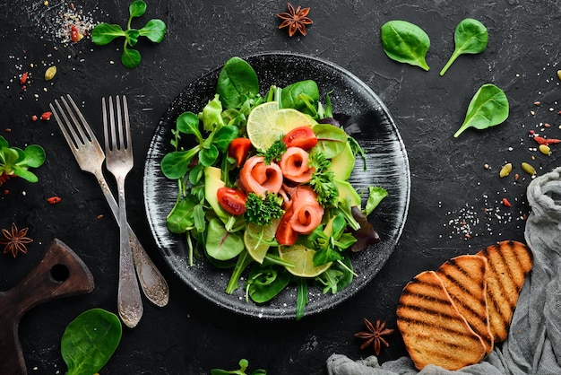 Salade au saumon, avocats, tomates et épinards Dans une assiette noire sur un fond en bois Vue de dessus Espace libre pour votre texte Mise à plat