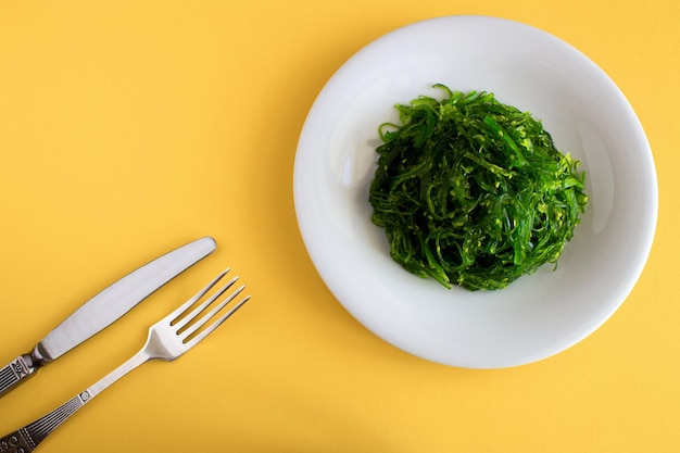 Salade aux algues et sésame dans l'assiette blanche sur fond jaune. Vue de dessus.