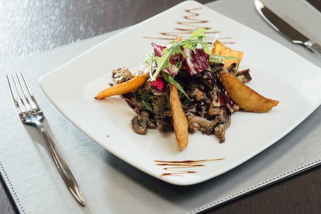 Salade aux champignons frits, pommes de terre frites, verts sur une assiette sur la table