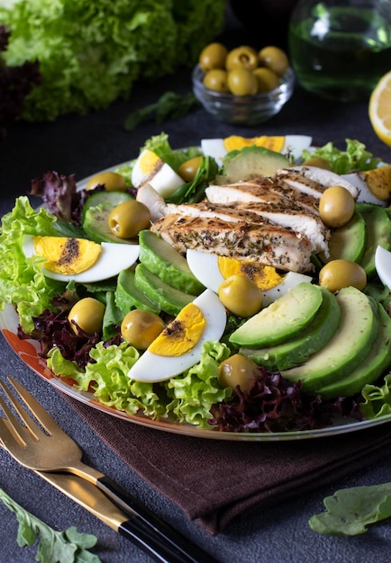 Salade aux œufs de poulet à l'avocat et aux olives habillées de citron et d'huile d'olive servies sur des feuilles de laitue sur fond gris