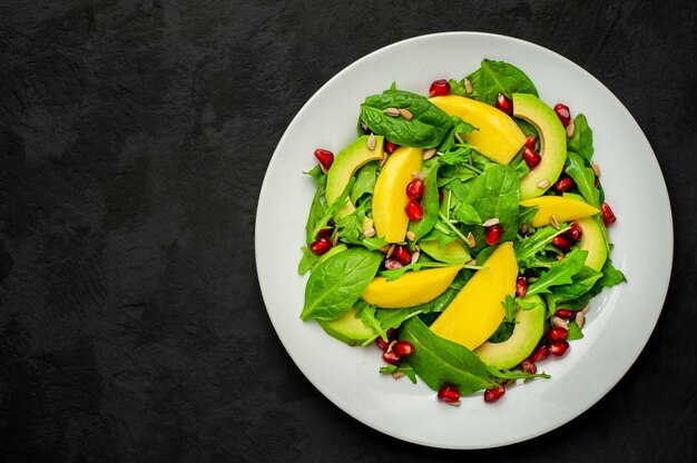 Salade d'avocat aux épinards et à la grenade sur une plaque blanche sur une pierre noire