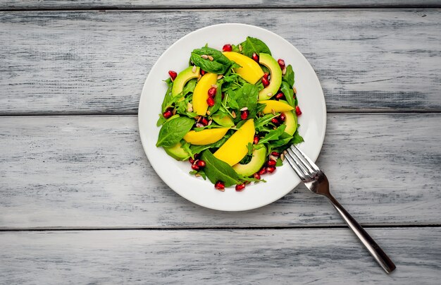 Salade d'avocat aux épinards et à la grenade sur une plaque blanche sur une table en bois