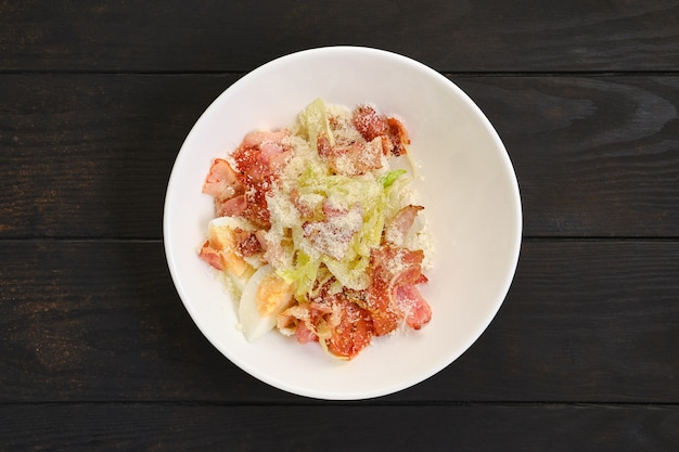 Salade de bacon, oeuf, chou et fromage râpé sur table en bois foncé