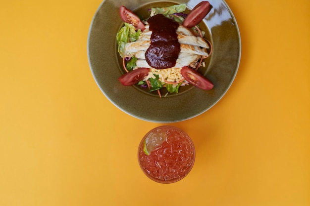 Salade barbecue, avec filet de poulet, laitue romaine, tomates sur une assiette sur fond jaune.