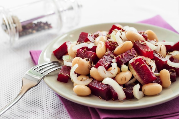 Salade de betteraves rouges aux haricots blancs, cornichons et oignons, assaisonnée d'huile et parfumée aux graines de carvi