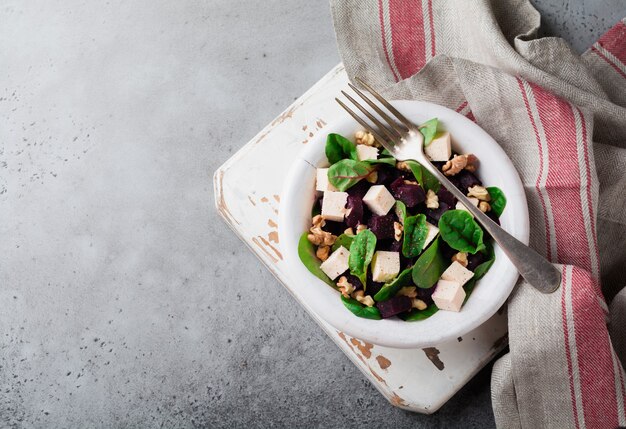 Salade de bettes, roquette, betterave, ricotta et noix à l'huile d'olive dans une vieille assiette en céramique sur une pierre grise ou béton vieilli fond