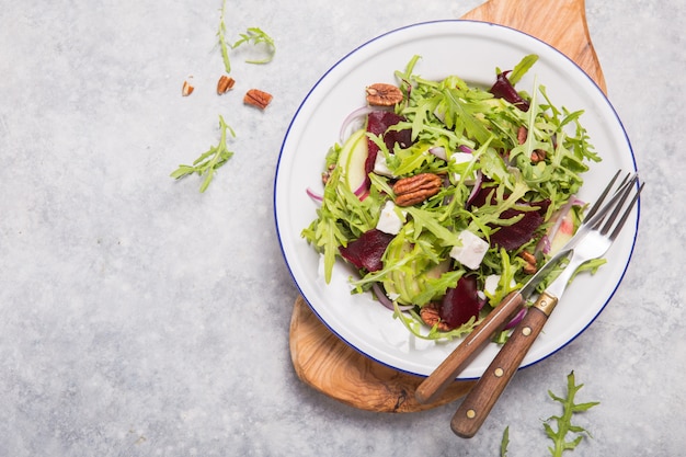 Salade biologique verte fraîche avec roquette, tranches de betterave, fromage feta, noix, pomme sur plaque blanche, vue de dessus. Une alimentation saine, un régime amaigrissant concept